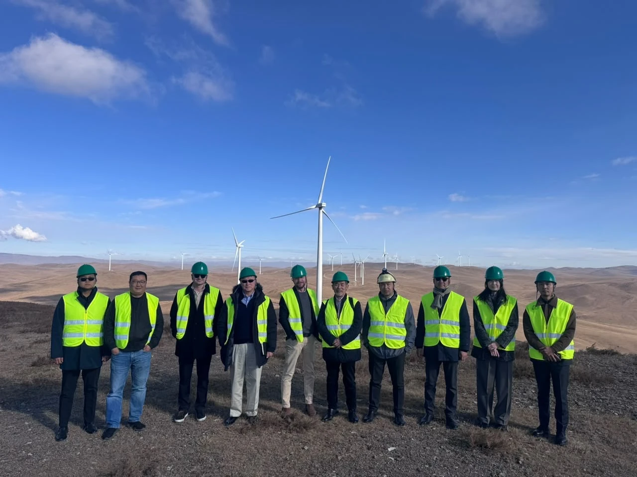 Site visit team in hard hats and safety vests in front of wind turbines, Mongolia